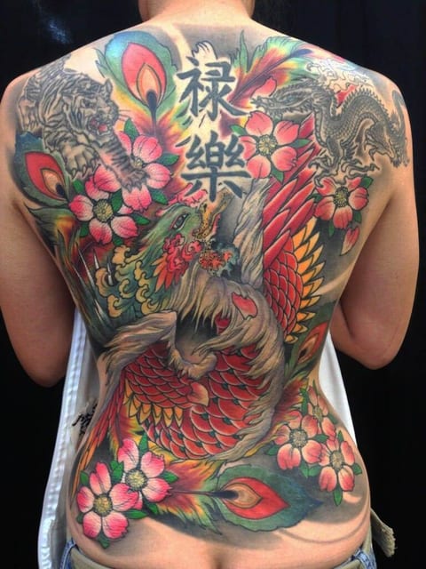 A colorful Japanese phoenix, tiger, dragon and blossoms cover a person's back.