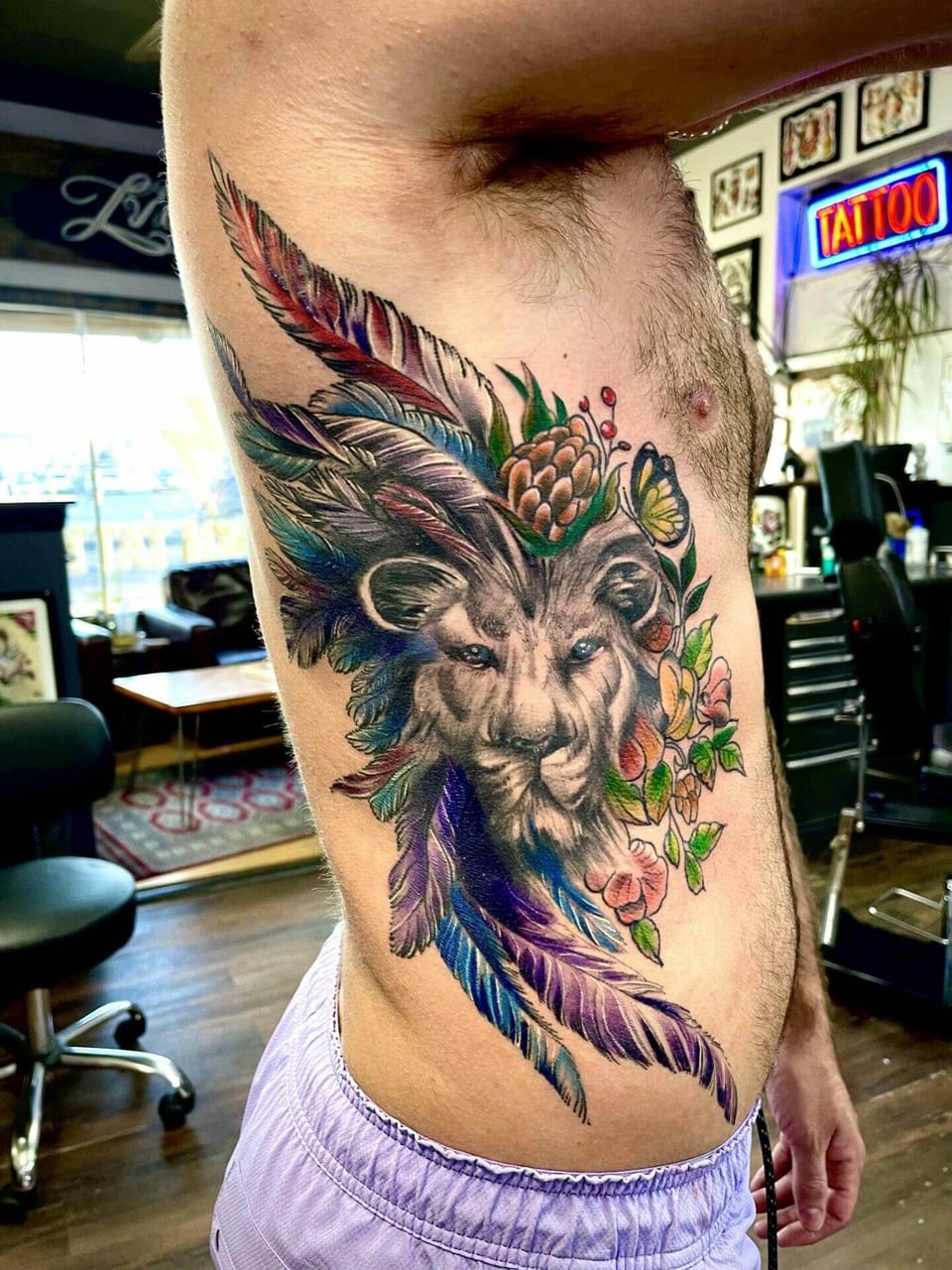 A color lion portrait with feathers, flowers and a butterfly covers the ribs.