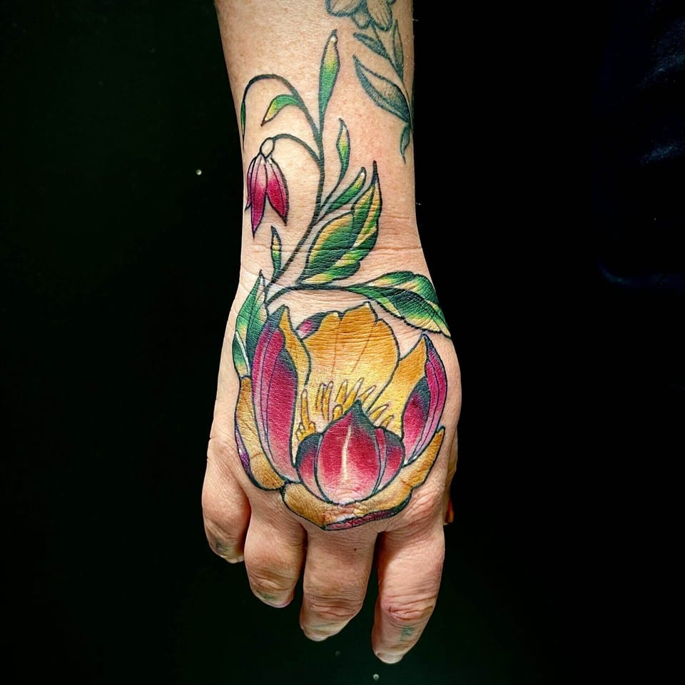 A pink and yellow neo traditional flower covers the back of a hand and extends up the wrist.