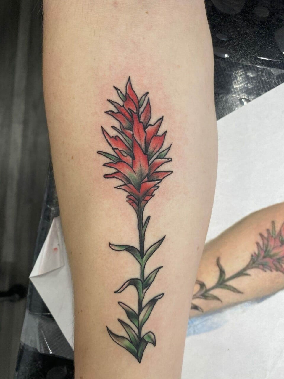 A red illustrative flower with green leaves runs along the inner forearm.