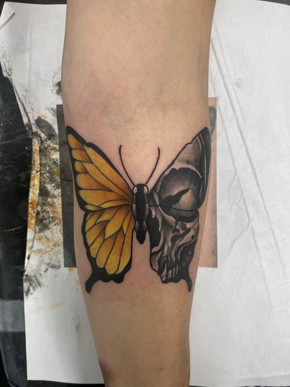 An illustrative butterfly with a yellow wing and a skull-shaped wing sits on a forearm.