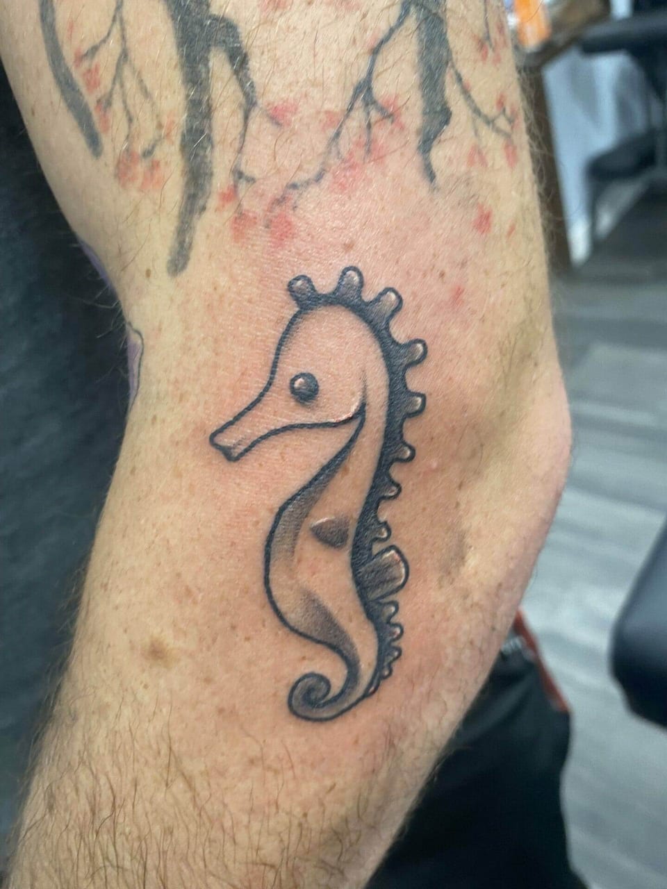 A small black illustrative seahorse with a curled tail sits on a forearm.