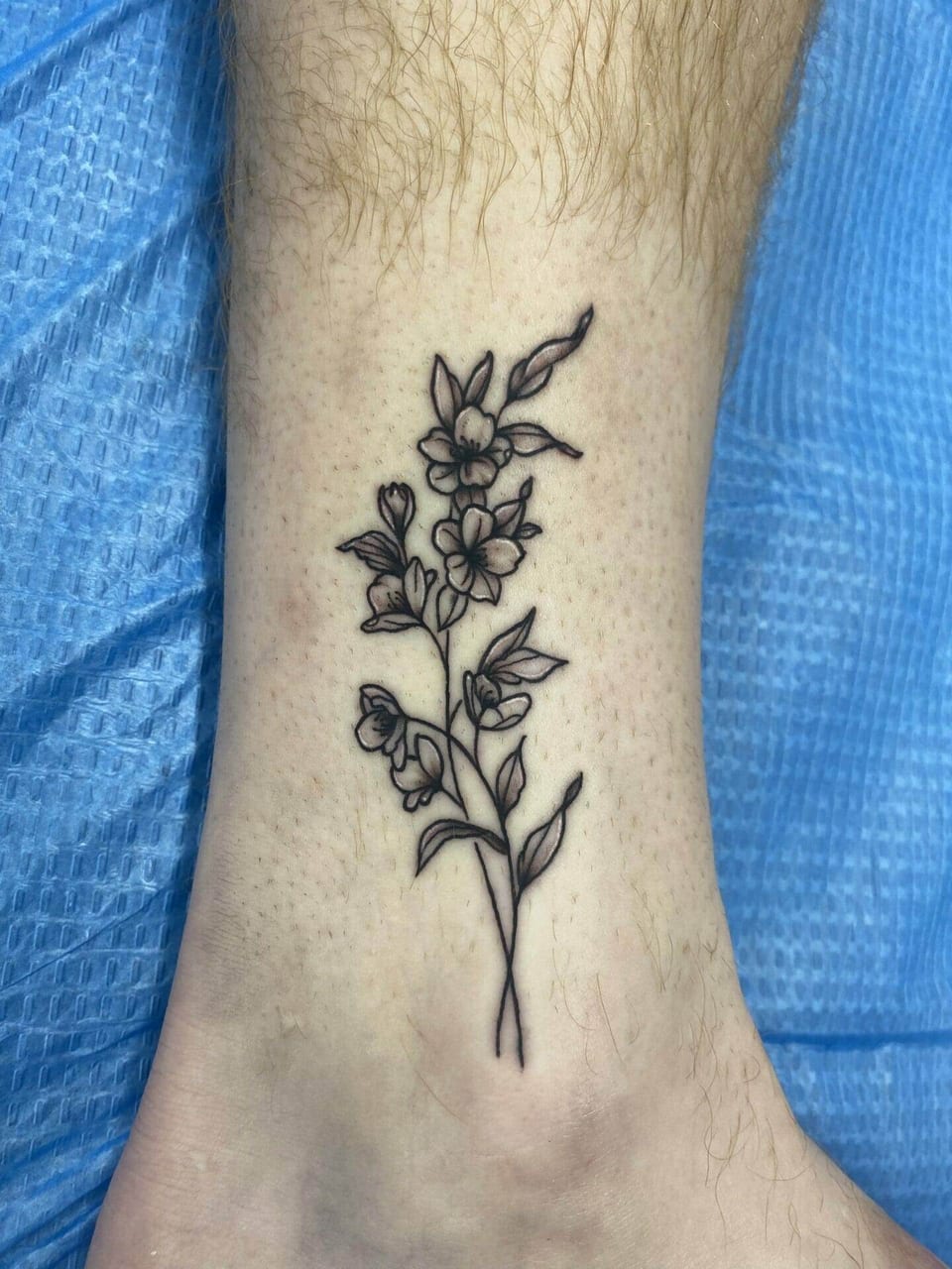 A black linework flowering sprig sits above the inner ankle.