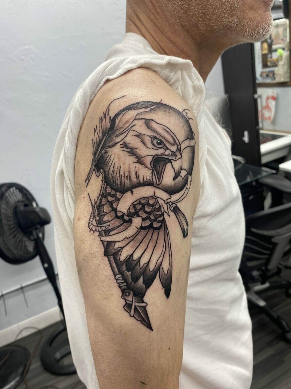 A black and grey illustrative eagle with a spear and feather covers an upper arm.