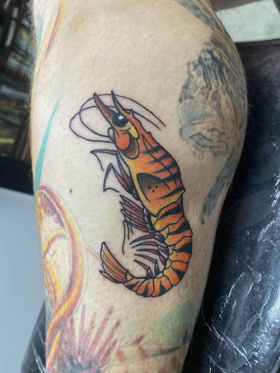 A traditional orange shrimp tattoo sits on an upper arm.