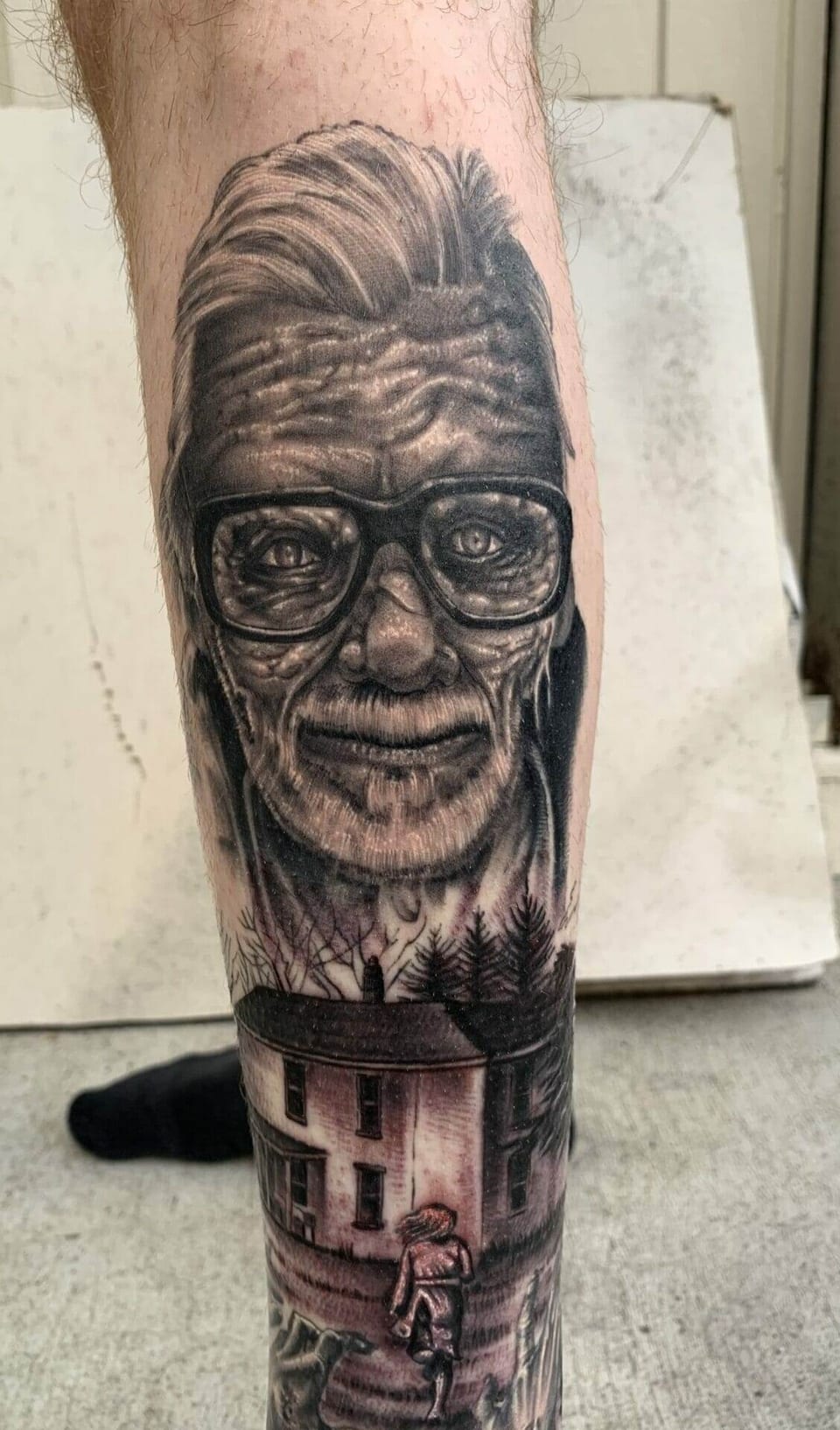 A black and grey horror portrait rises above a house and walking figure on the calf.