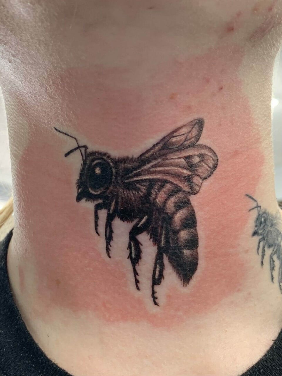 A black and grey bee tattoo sits on the front of the neck.