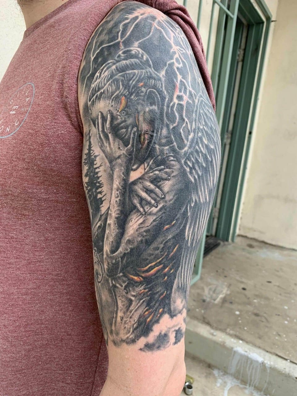 A black and grey winged woman with glowing orange cracks covers the upper arm.