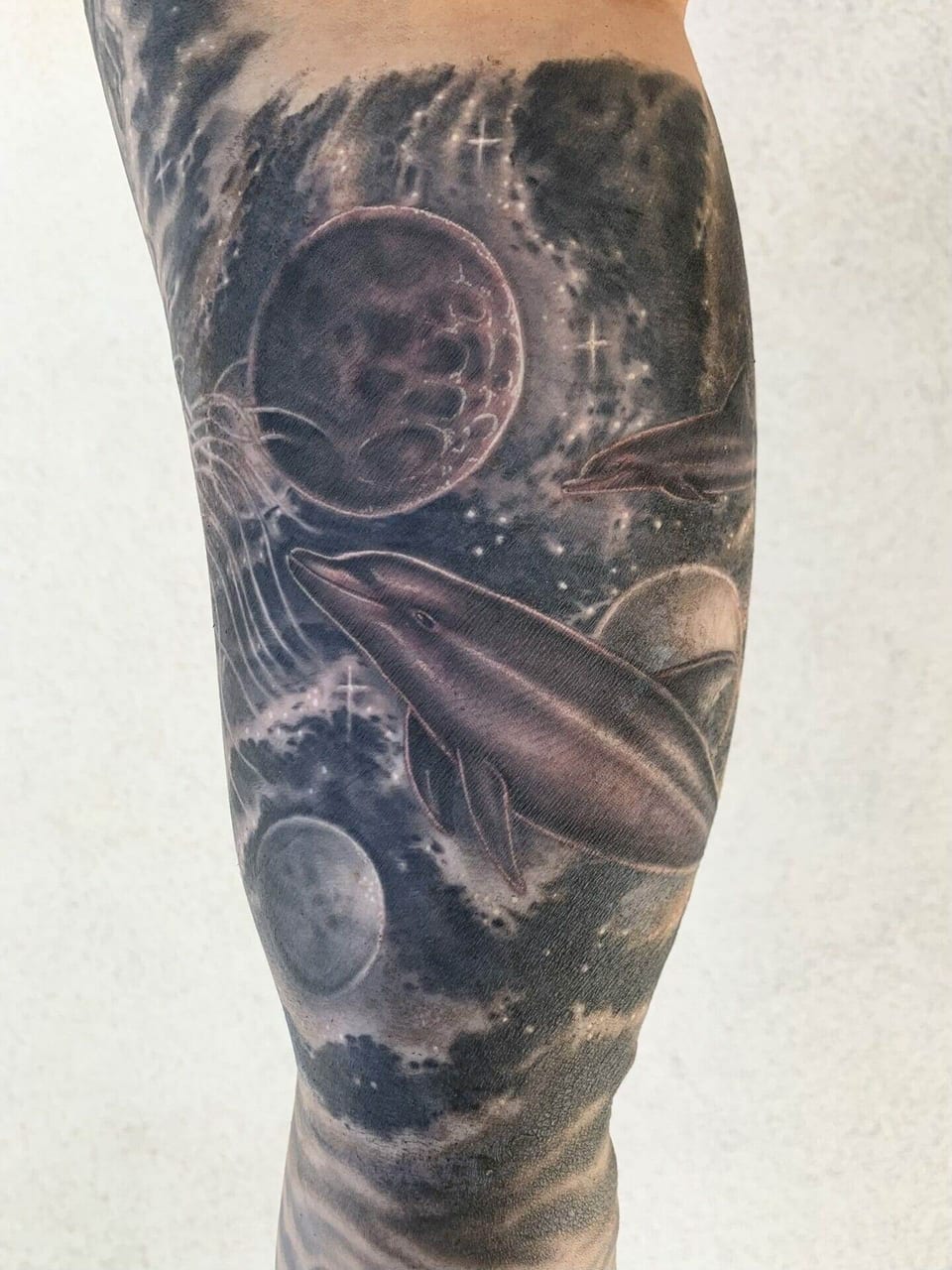 Black and grey dolphins, jellyfish and planets fill a forearm tattoo.