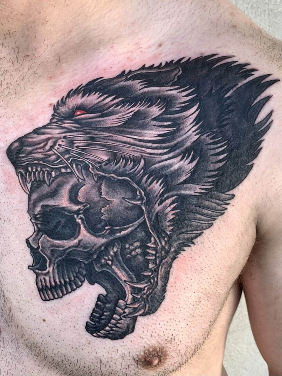 A black and grey wolf head surrounds a skull on the chest.