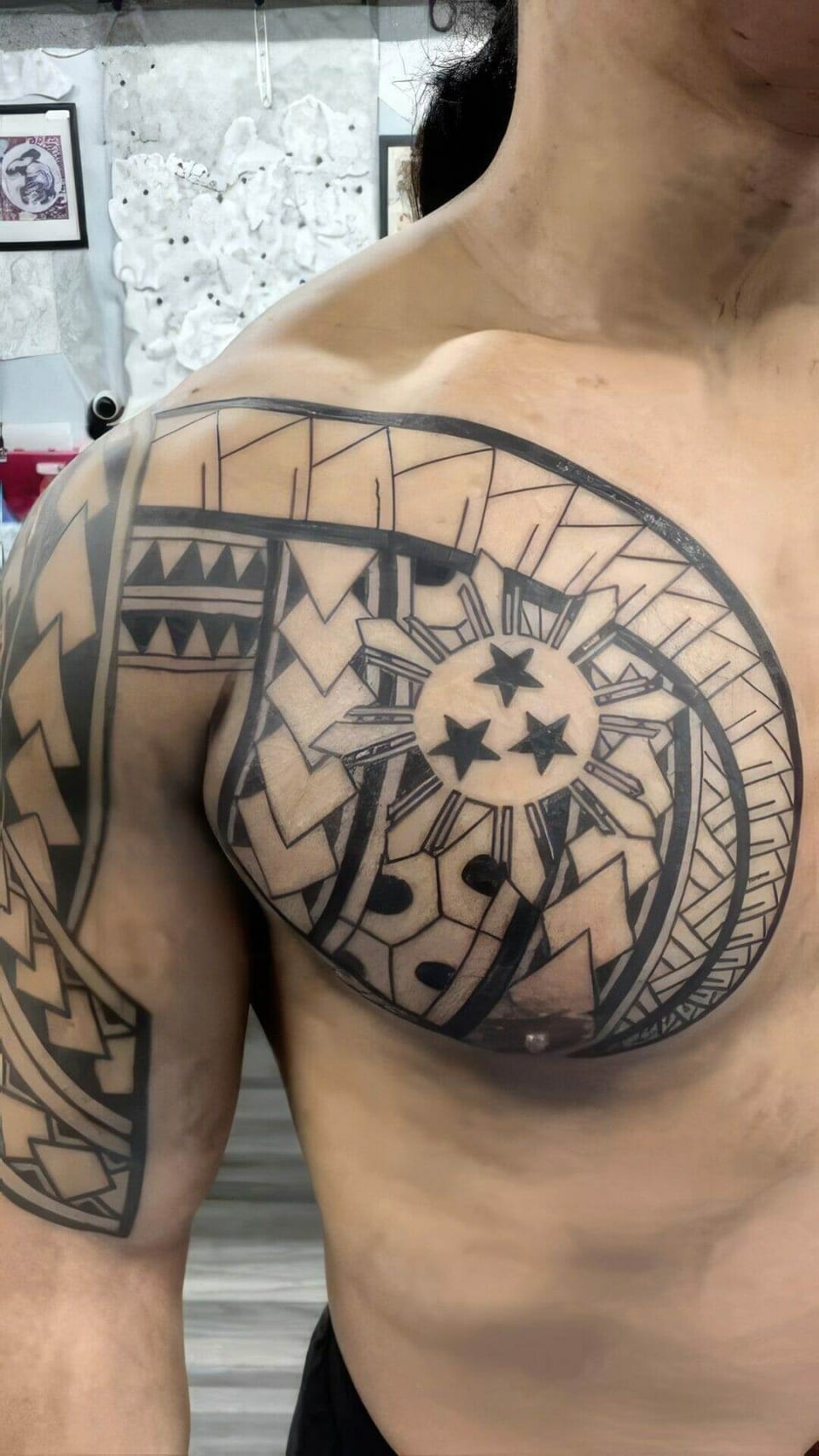 Black Polynesian geometric patterns surround a sun and stars on the chest and upper arm.