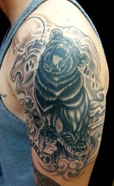 A black and grey roaring bear stands against mountains and clouds on the upper arm.