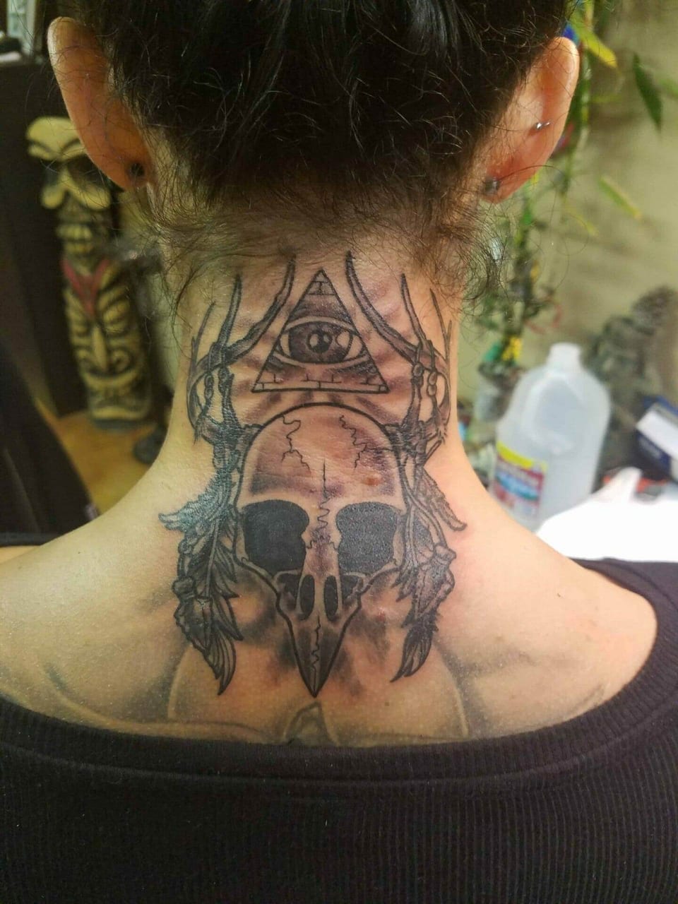 A black and grey bird skull, antlers and an eye in a triangle cover the back of the neck.