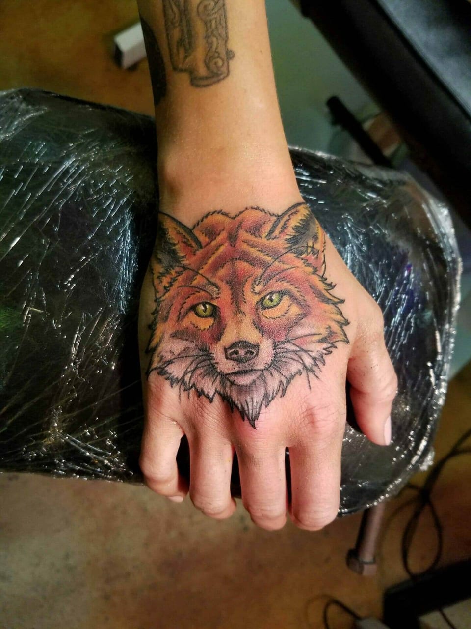 A color fox portrait with yellow eyes covers the back of the hand.