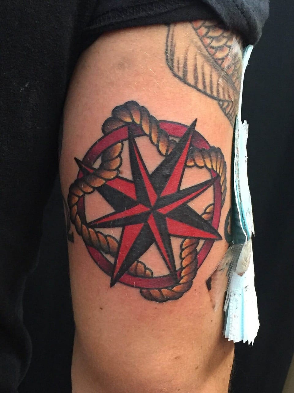 A traditional red and black nautical star sits inside a rope-wrapped red ring on the upper arm.