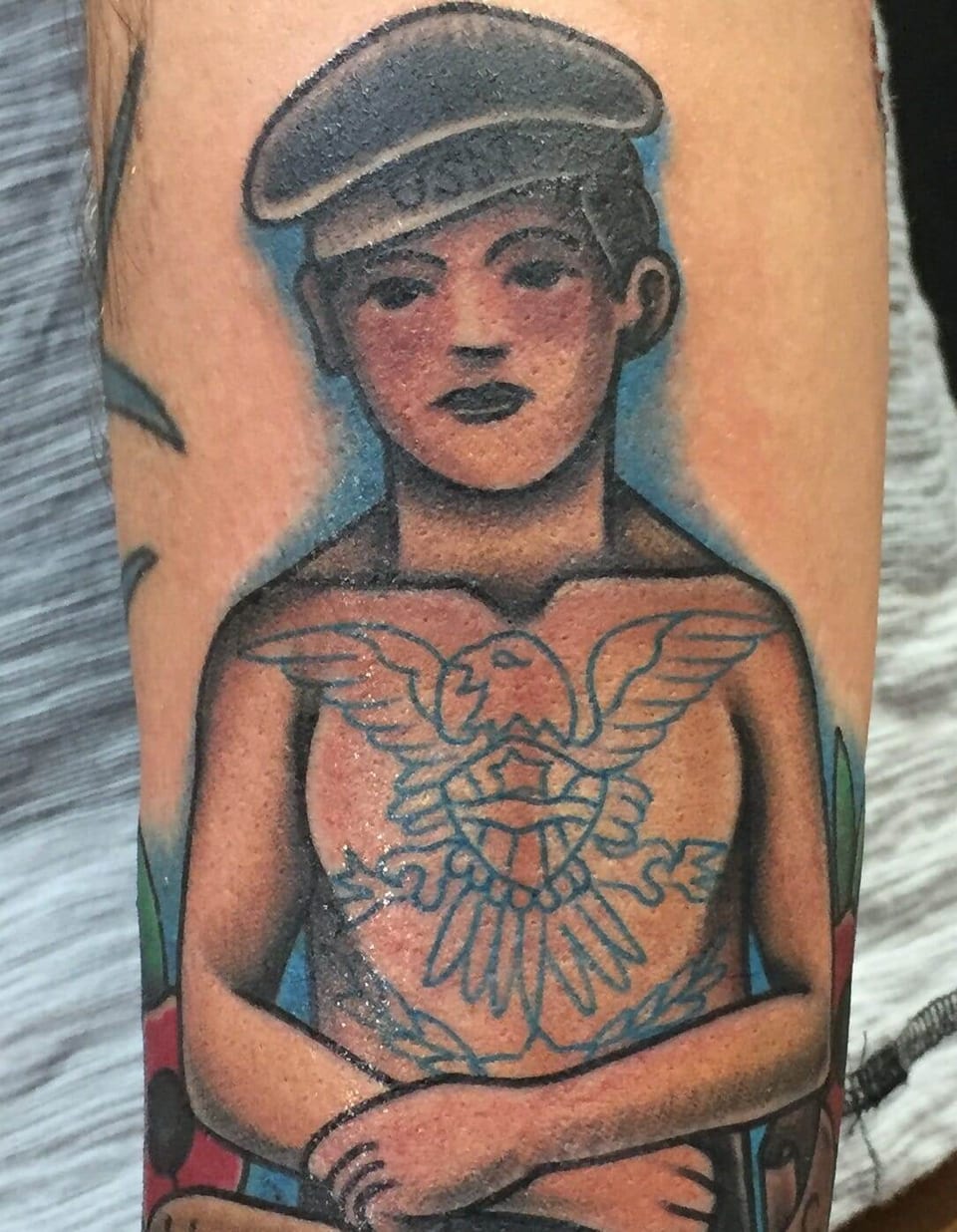 A traditional sailor portrait with an eagle on the illustrated chest covers the forearm.