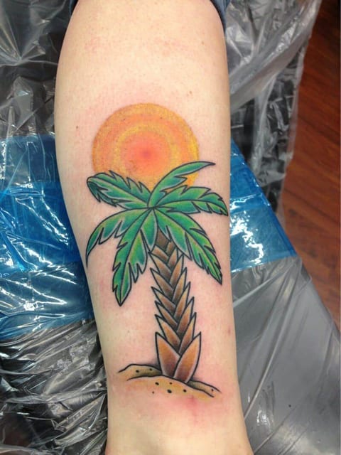 A traditional green palm tree stands beneath an orange sun on the forearm.