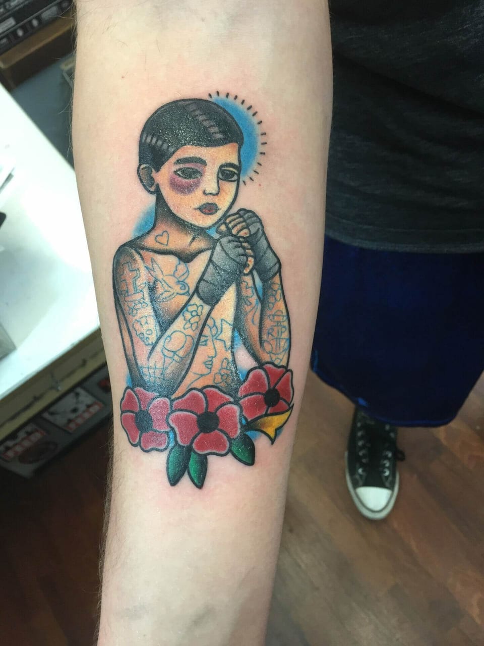 A traditional boxer with wrapped fists and a black eye stands above red flowers on the forearm.