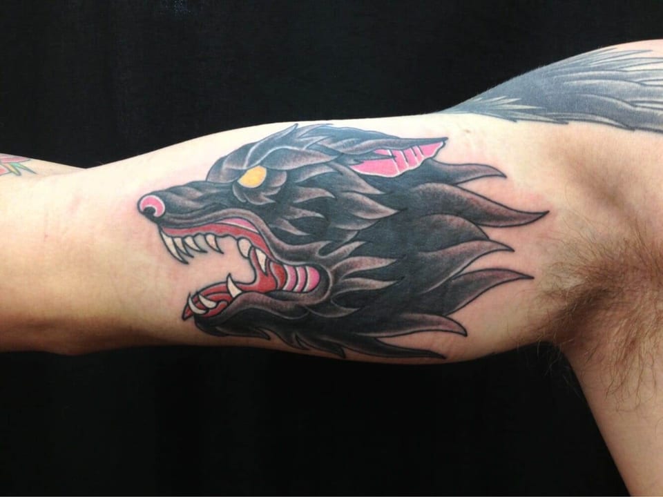 A traditional black wolf head with yellow eyes and red accents snarls on the inner upper arm.