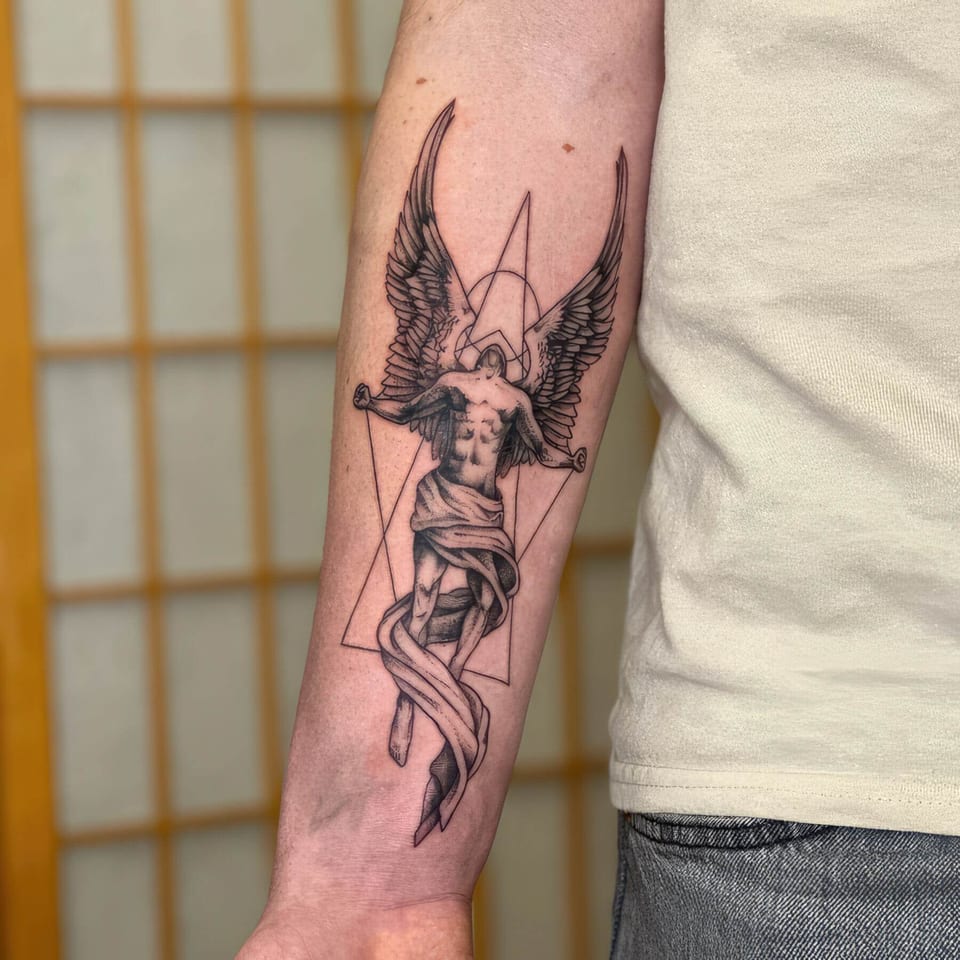 A fine-line winged figure with draped cloth rises inside geometric outlines on the forearm.