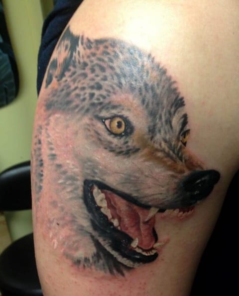 A realistic grey wolf with yellow eyes and open jaws fills the upper arm.