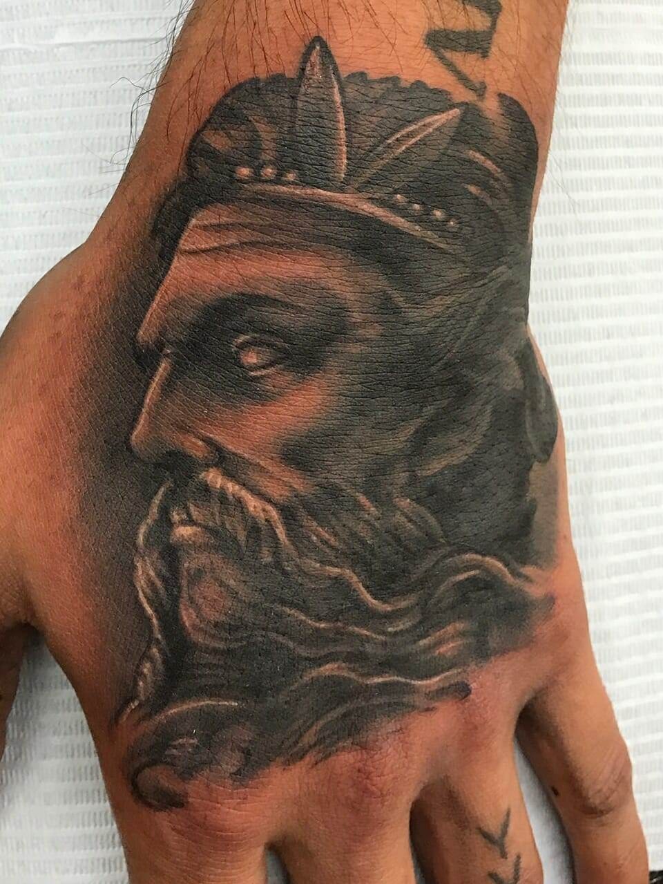 A realistic black and grey bearded king in a crown fills the back of the hand.
