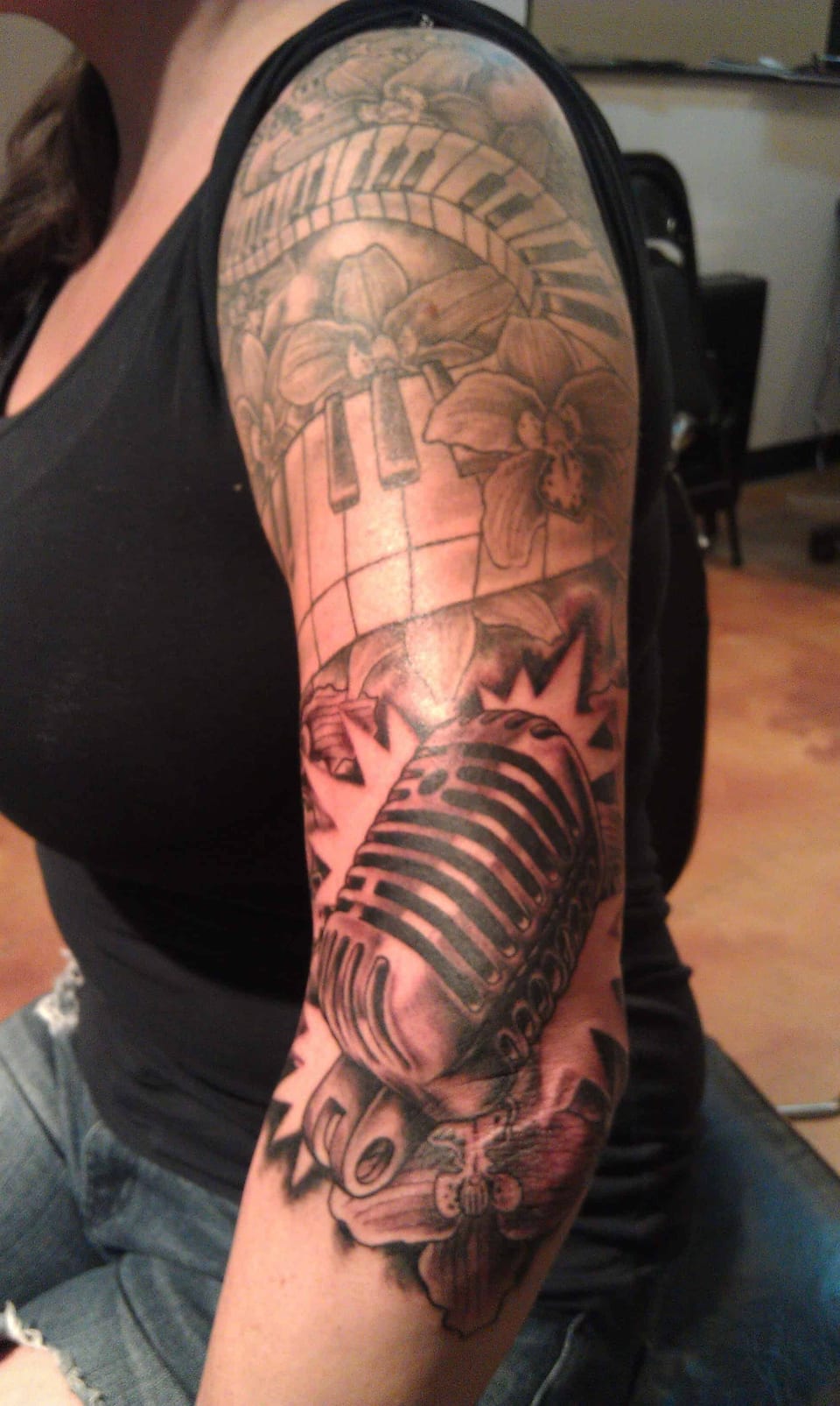 A black and grey sleeve combines curved piano keys, orchids and a vintage microphone on the upper arm.