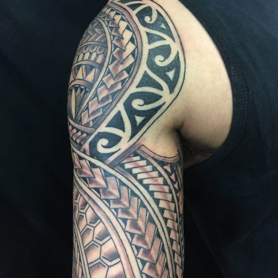 Black Polynesian bands with spirals, chevrons and hexagons extend from the shoulder down the upper arm.