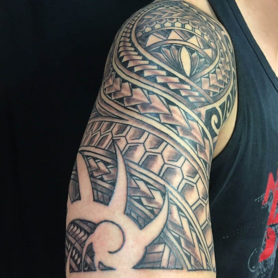 A black Polynesian upper-arm tattoo combines a sun motif, geometric bands and broad uninked curves.