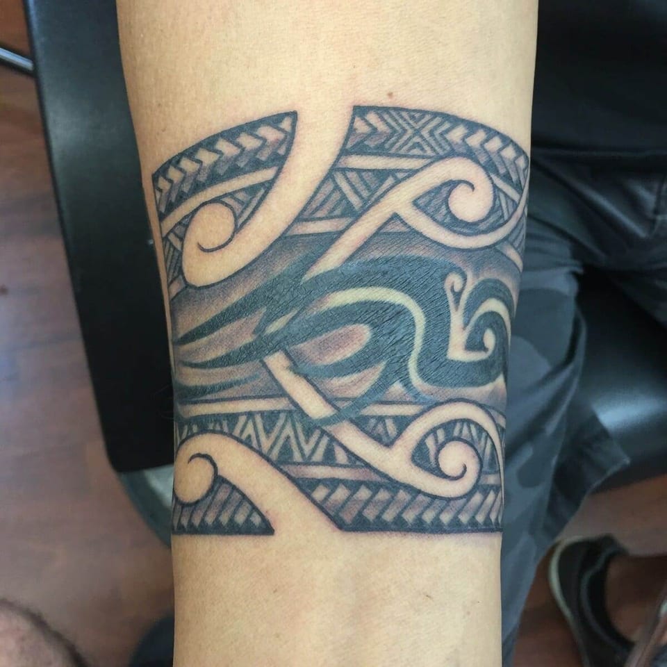 A black Polynesian arm band combines bold waves, uninked curls and triangular borders.