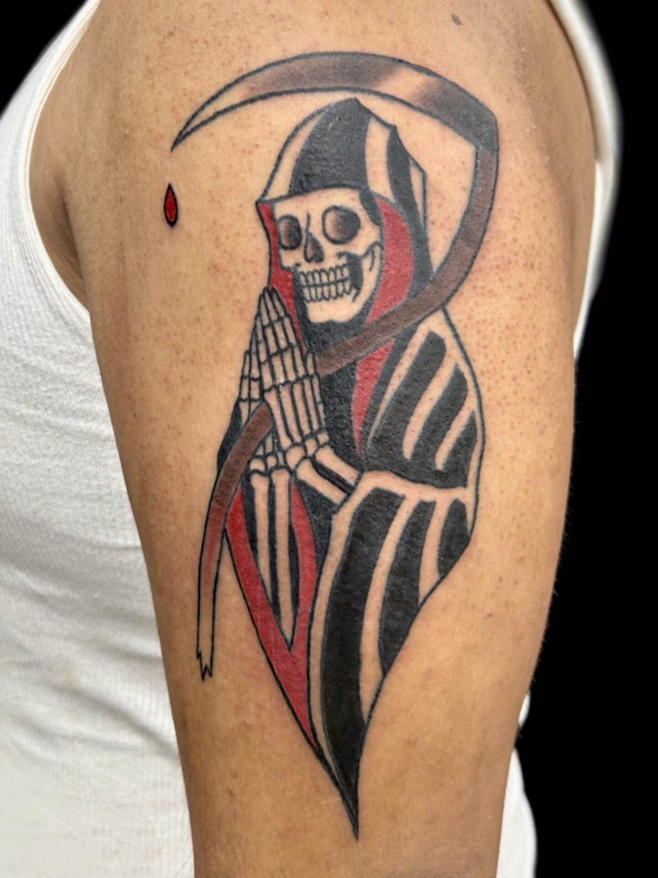 A traditional grim reaper in a red and black cloak holds a scythe beside praying hands on the upper arm.