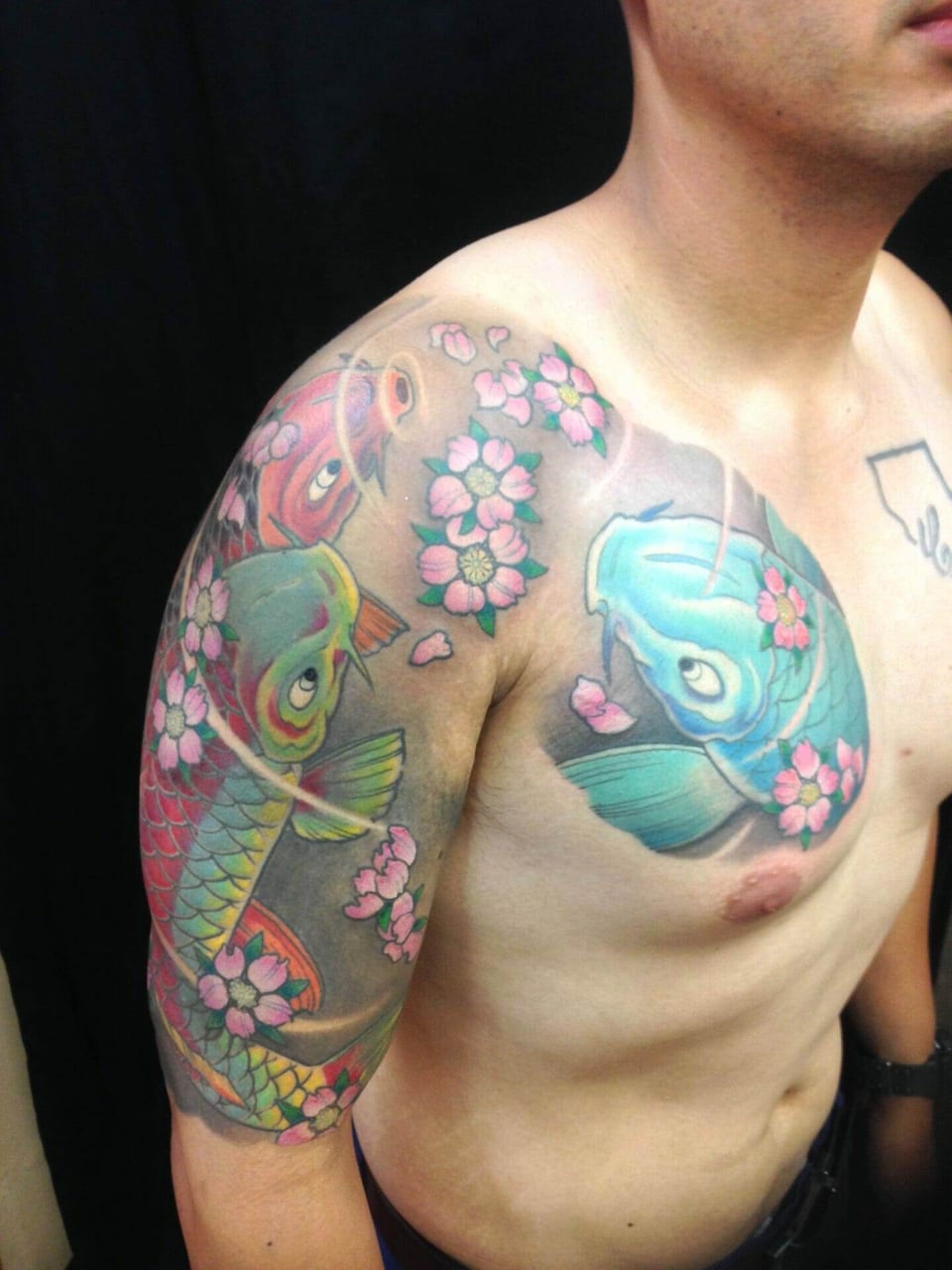 A Japanese koi tattoo combines blue, green and red fish with pink cherry blossoms on the chest and upper arm.