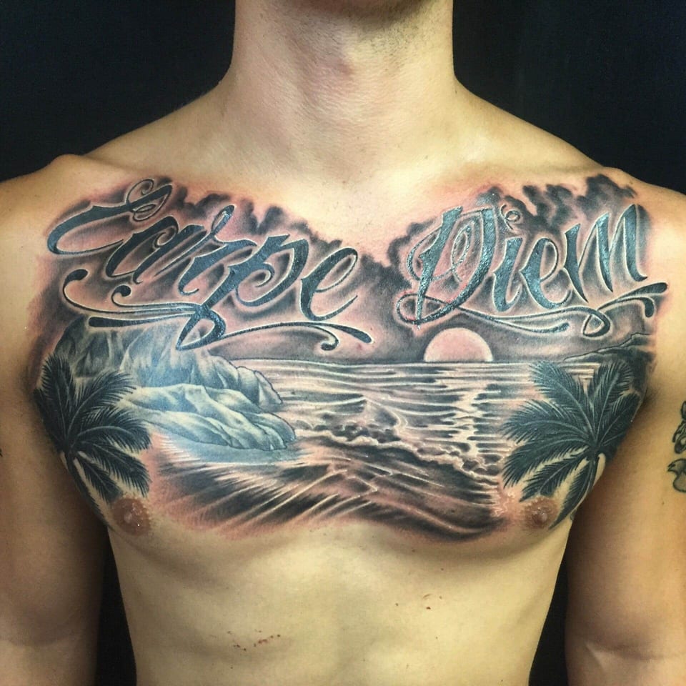 A black and grey beach tattoo places palms and a sunset beneath Carpe Diem lettering across the chest.