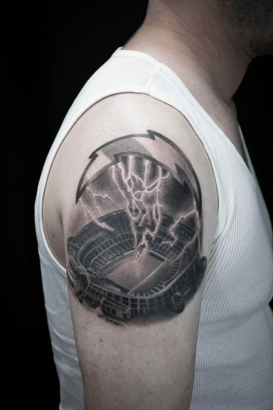A black and grey stadium beneath lightning sits inside circular arrows on an upper arm.