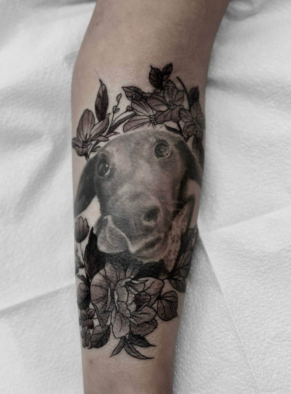 A black and grey dog portrait sits within flowers and leaves on a calf.