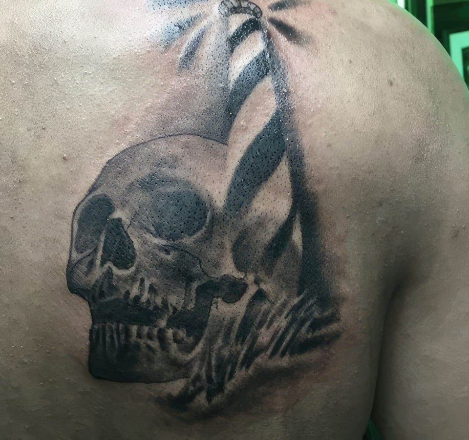 A black and grey skull sits beneath a striped lighthouse on the upper back.