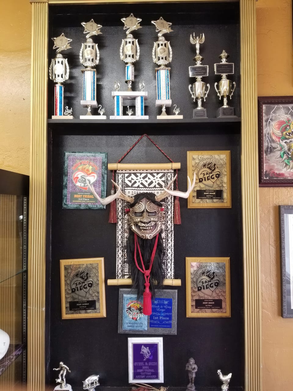 Trophies and plaques labeled "Best tribal" and "Best back" surround a horned mask on a shop display.