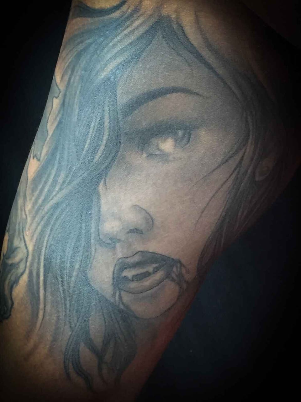 A black and grey woman with long wavy hair appears in a portrait tattoo on an arm.