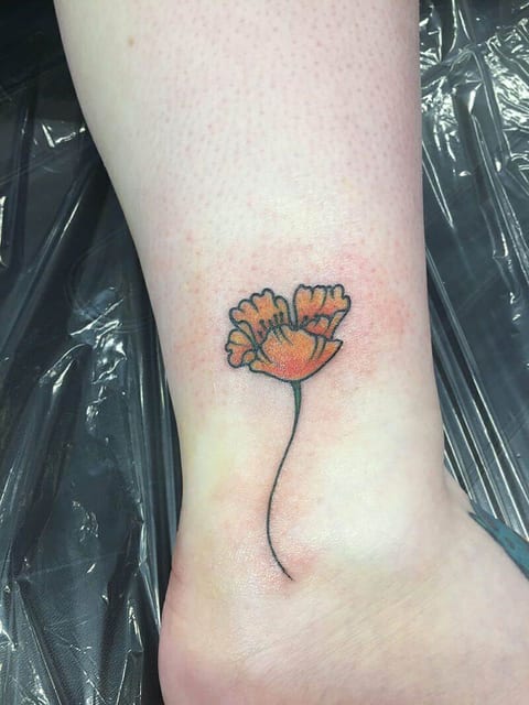 A fine-line orange poppy with a curved stem appears in a tattoo above the ankle.
