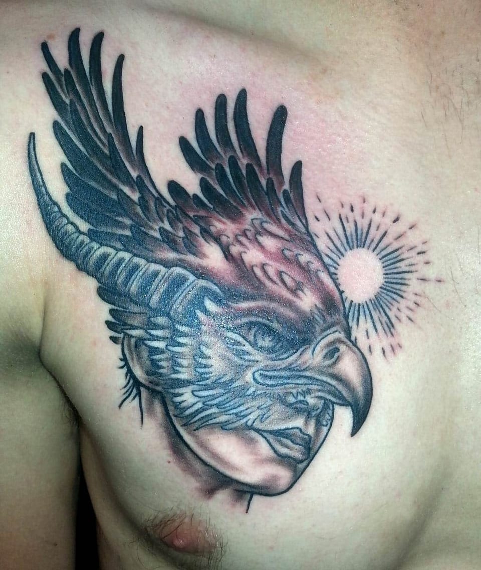 A black and grey eagle merges with a woman's face beneath a sunburst on the chest.
