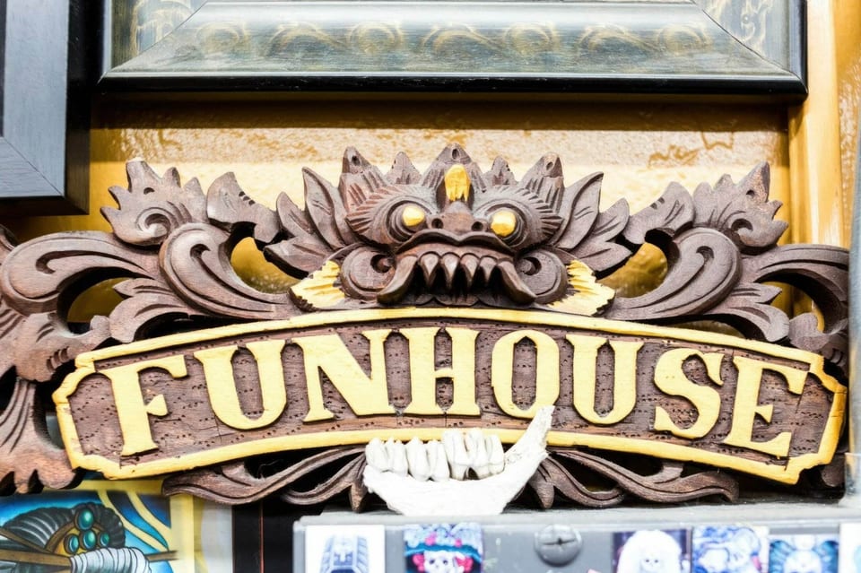 A carved wooden Funhouse sign features gold lettering beneath a fanged face.