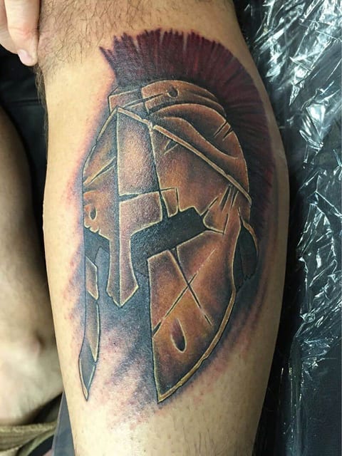 A bronze Spartan helmet with a red crest appears in an illustrative calf tattoo.