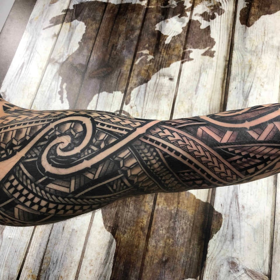 Polynesian forearm piece with spirals against a wooden map wall, tattooed by Seth Reynolds
