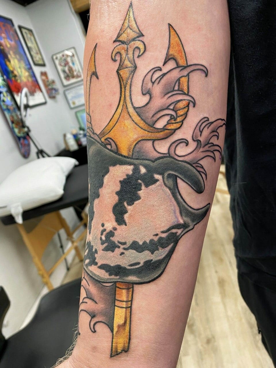 An angled view shows a neo-traditional gold trident, spotted manta ray and pink waves on the forearm.