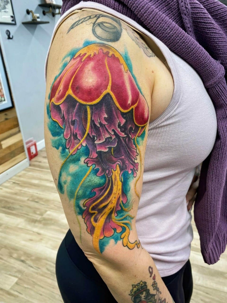 A neo-traditional pink jellyfish trails purple and gold tentacles against turquoise on the upper arm.