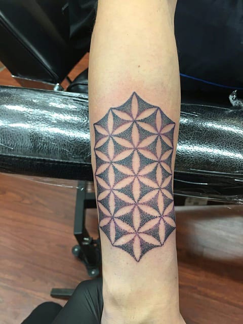 A stippled flower-of-life pattern forms a long geometric tattoo on a forearm.