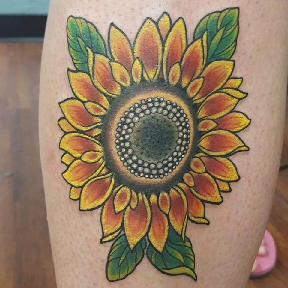 A close view shows a traditional color sunflower with a beaded center and green leaves on the calf.