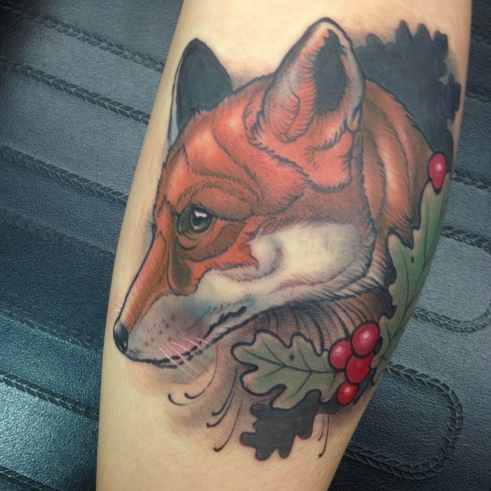 An orange fox head appears among green leaves and red berries on a forearm.