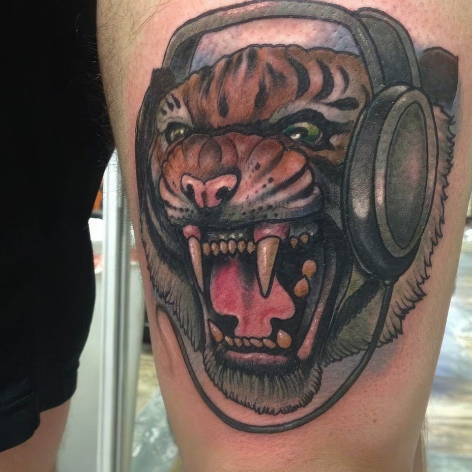 A neo-traditional roaring tiger wears large headphones on a cropped limb.