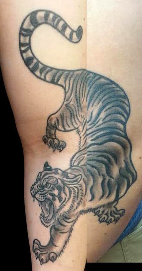 A black and grey Japanese tiger prowls down the inner upper arm with its mouth open and tail curled.
